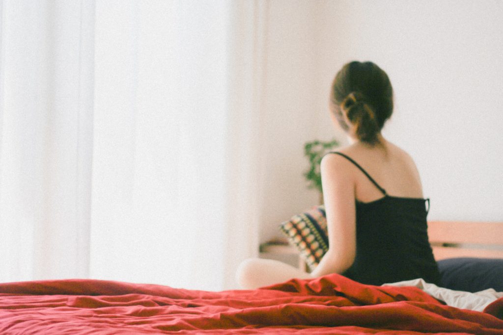 femme de dos assise sur un lit avec un drap rouge