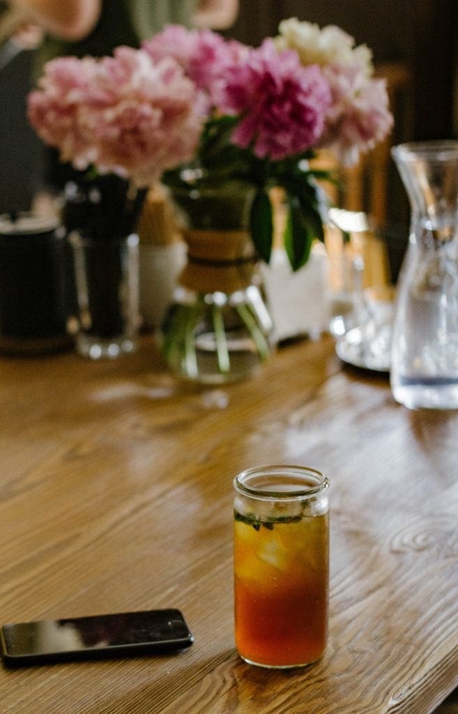 mason jar de thé glacé au puerh sur une table avec un vase de fleurs et un téléphone portable