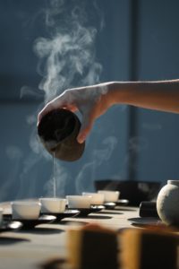 thé puerh dans des bols blancs, main qui sert de l'eau chaude dessus depuis un bol noir